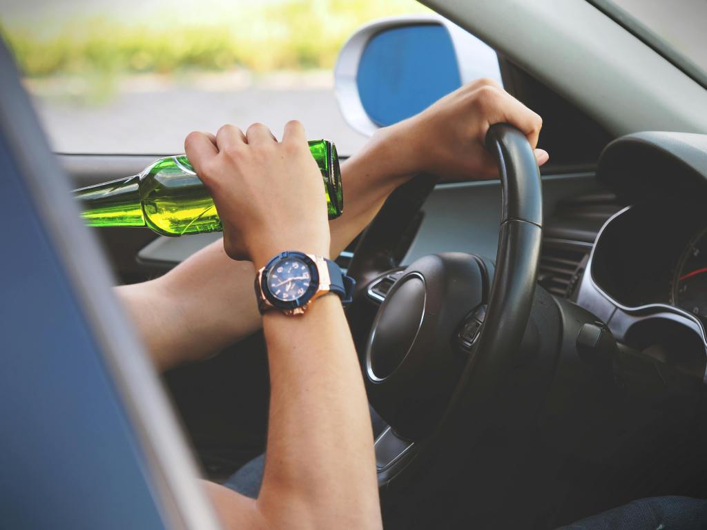 A man with a watch drinking a beer while driving a car. 