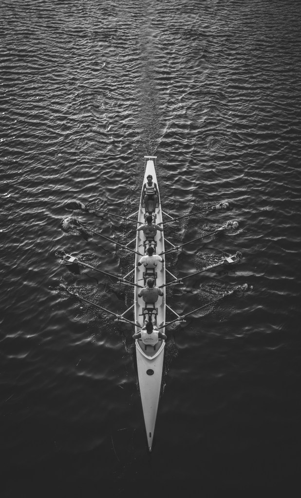 A black and white photo of a rowing team sailing on the ocean.