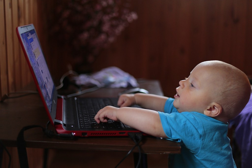 Studying like a baby. A baby is staring at a computer screen with it's hands on the keyboard. 