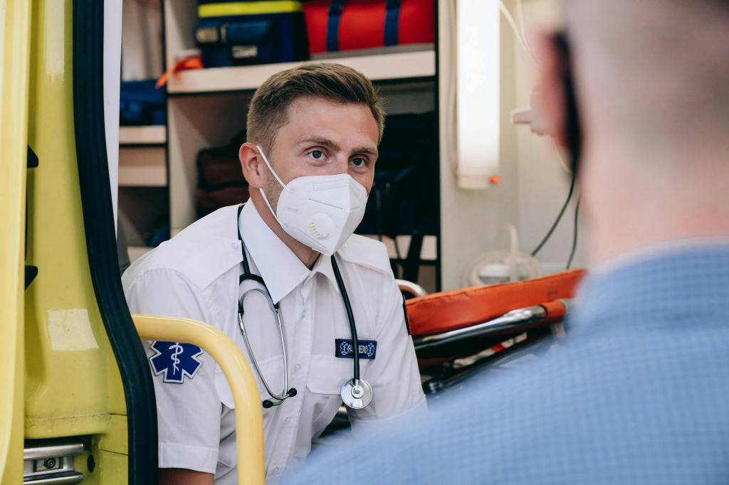 Paramedic sitting at the back of an ambulance assessing a patient. 