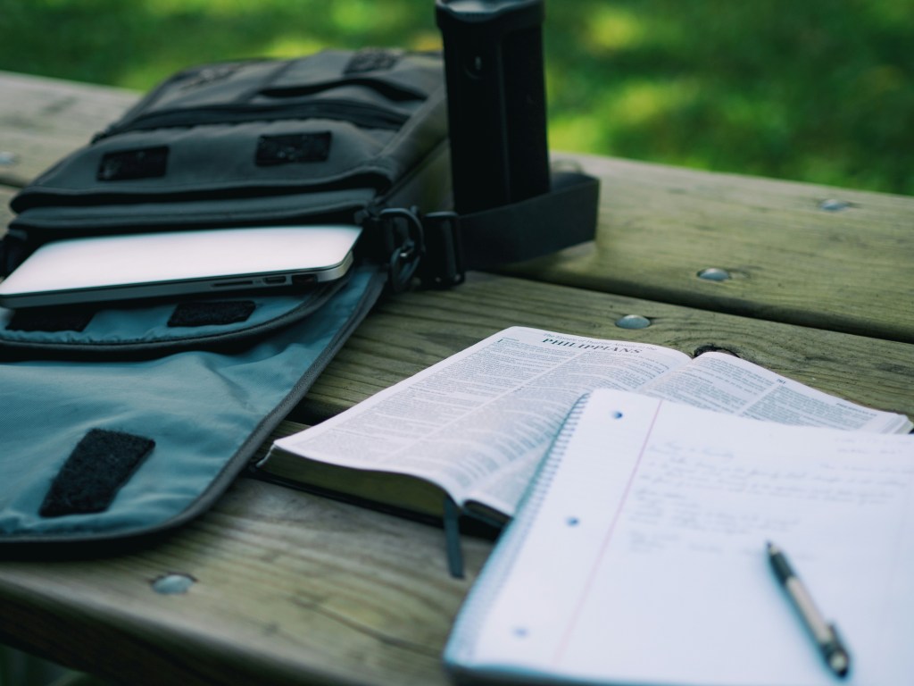 Paramedic study materials. there is a notebook with a pen and a tactical bag on the left hand side of the bench the student is studying on. 
