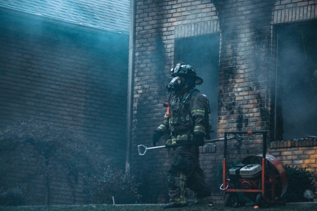 A firefighter walking out of a building after a fire. He is in all of his turnout gear. 