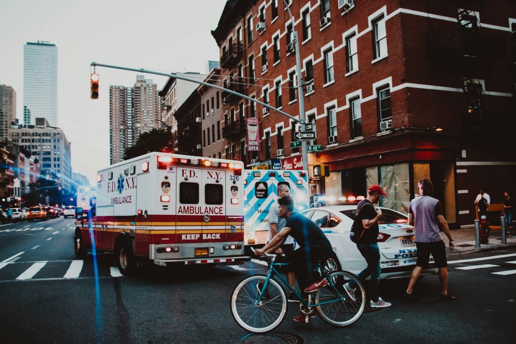 Two ambulances on a busy street with pedestrians walking by. 