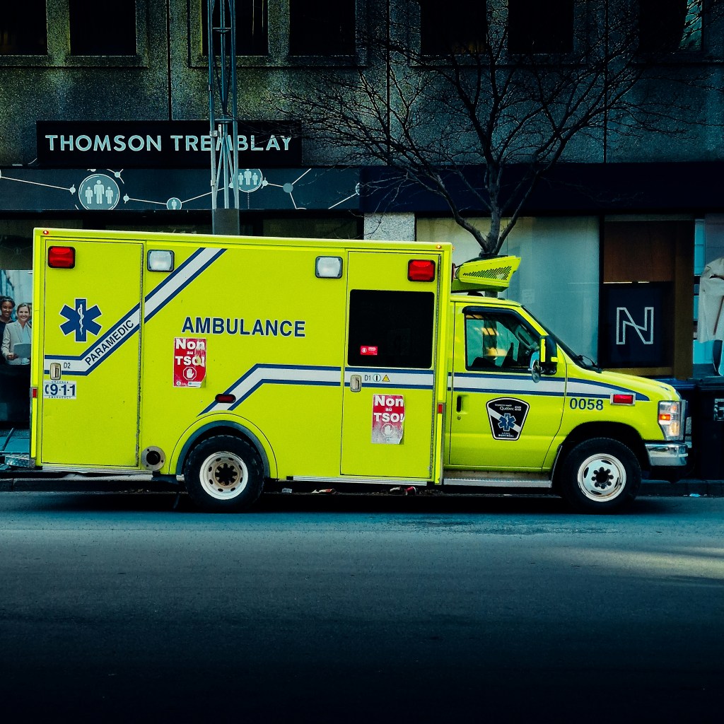 A bright yellow ambulance parked in front of a building on the street. 