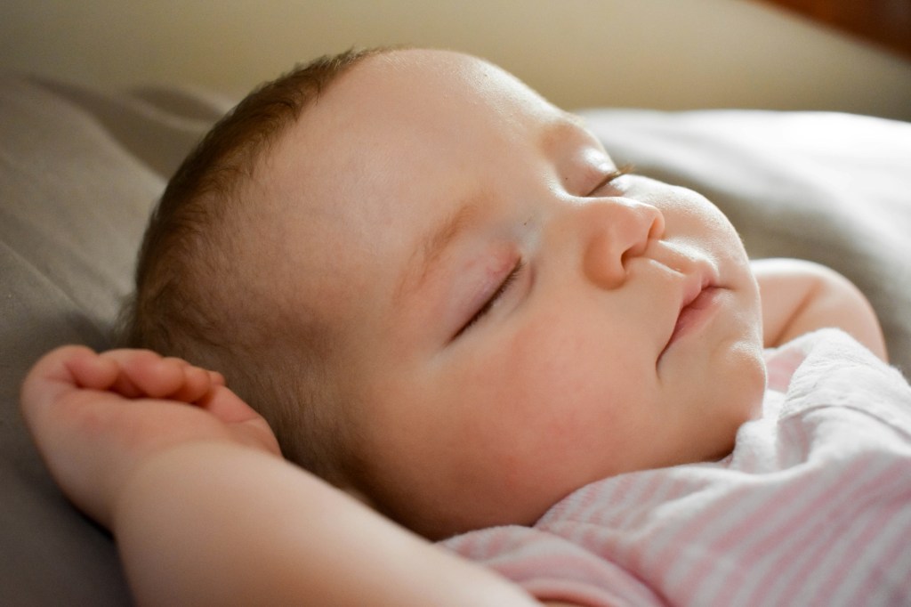 An infant sleeping with his hands up. 
